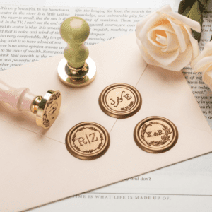 Two decorative wax seals and stamps in pink and green, arranged on a light paper background with a cream rose.